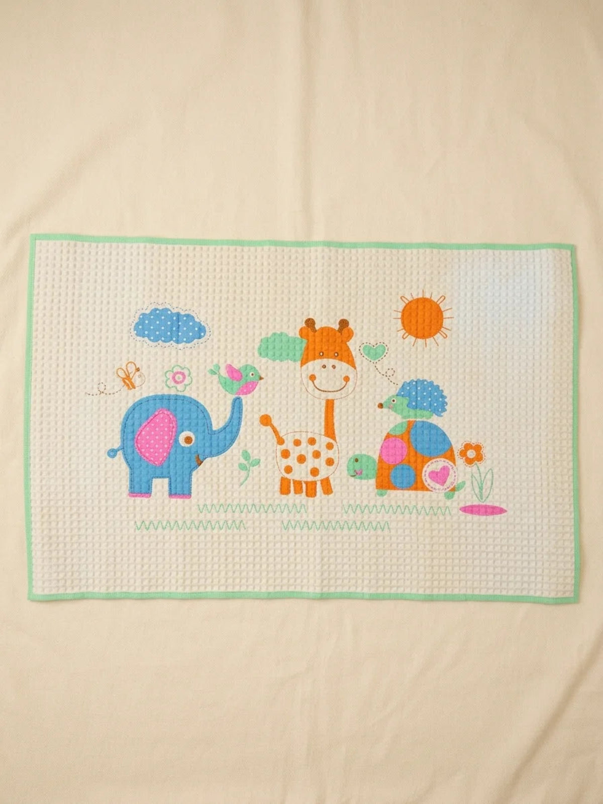 Safari Friends quilted baby play mat showing blue elephant orange giraffe and colourful turtle with sunshine clouds and flowers on cream background with mint green border