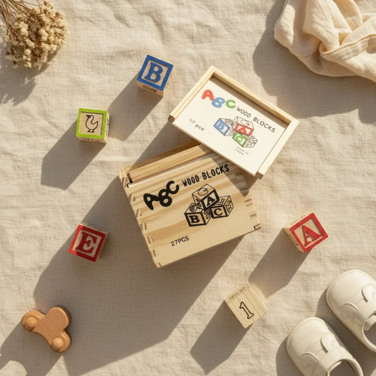 ABC Wood Blocks 27 piece set flat lay showing engraved pine wooden crate open with colourful letter blocks B red A green duck and number 1 block scattered on linen background with wooden toy car white baby shoes and dried flowers