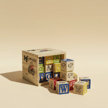 ABC Wood Blocks 27 piece set tumbling out of engraved pine wooden crate showing colourful letter blocks T O A M W C and animal illustration blocks on warm beige studio background