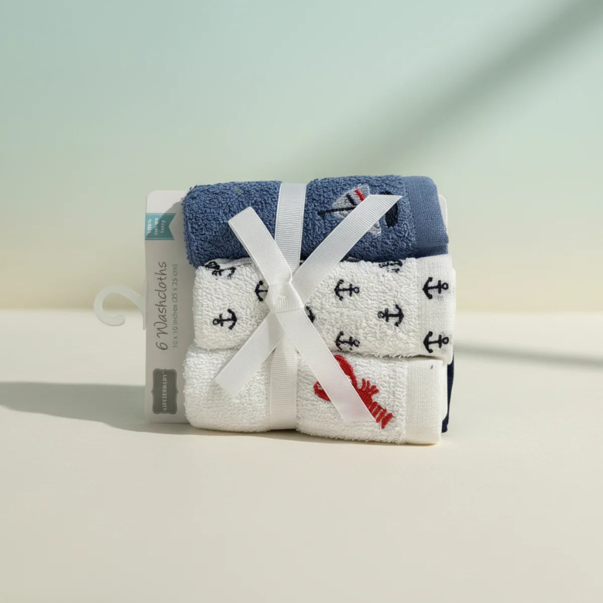 Nautical baby washcloths 6 pack bundled with white ribbon bow on retail hanger card showing navy blue terry top with sailboat motif white anchor print washcloths and red lobster embroidery cloth on soft teal cream studio background