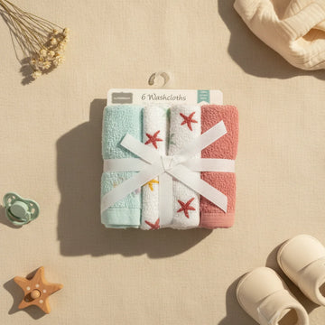 Starfish baby washcloths 6 pack flat lay from above on linen background showing Alfeer Baby hanger card with mint green white red starfish embroidery and dusty rose terry cloths bundled with white grosgrain ribbon bow with sage pacifier wooden starfish teether cream muslin swaddle and cream baby booties
