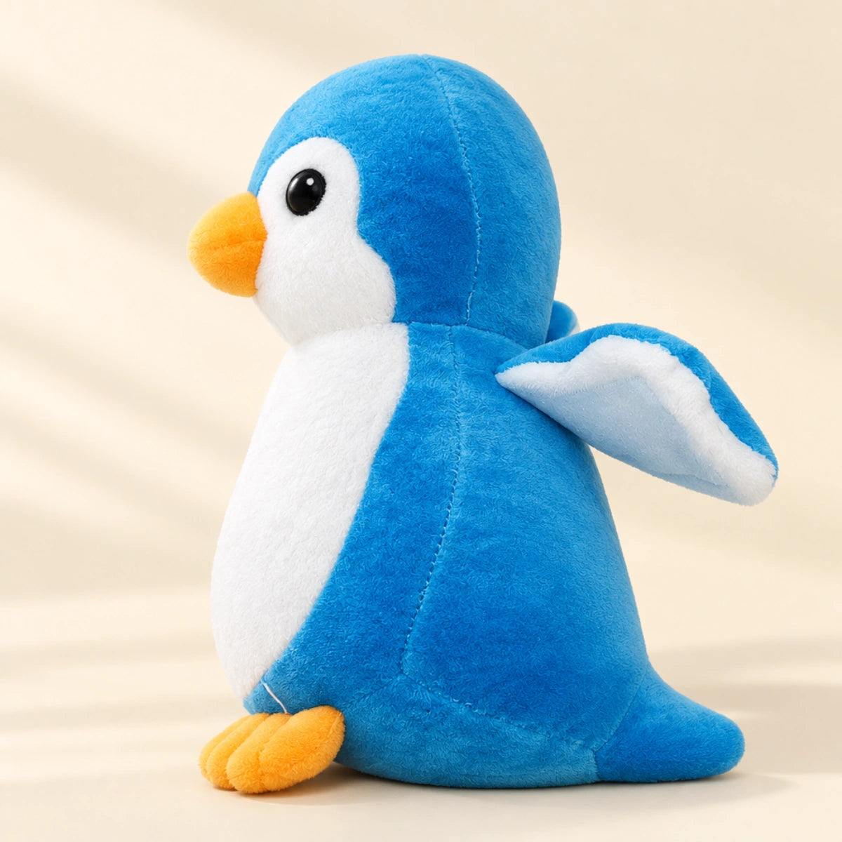 Blue penguin plush toy viewed from the side in a softly lit studio
