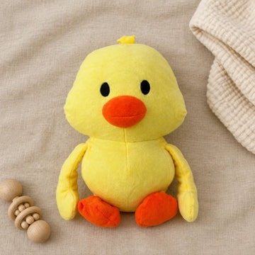 Yellow duck plush toy on neutral beige bedding beside a wooden toy
