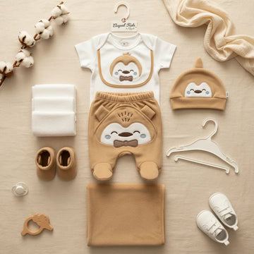 Elegant Kids Penguin Newborn Gift Set brown camel 7-piece flat lay showing bodysuit footed trousers penguin hat bib booties blanket and muslin cloth on linen background with cotton stems pacifier and white sneakers