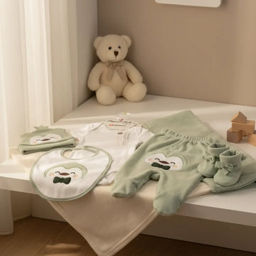 Elegant Kids Penguin Newborn Gift Set sage green lifestyle nursery scene showing hat bib bodysuit footed trousers booties and blanket draped on white nursery shelf with cream teddy bear and wooden building blocks