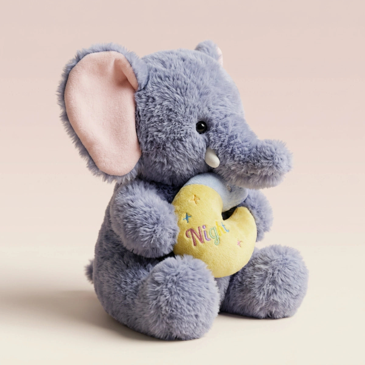 Grey elephant plush with pink-lined ears holding a yellow crescent moon cushion