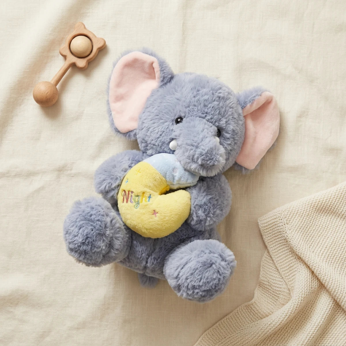 Grey elephant plush holding a yellow moon cushion on ivory linen