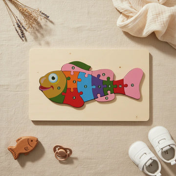 Colourful wooden fish jigsaw puzzle with numbered pieces 1 to 11 on natural wood board on linen background with wooden fish teether pacifier and white baby shoes