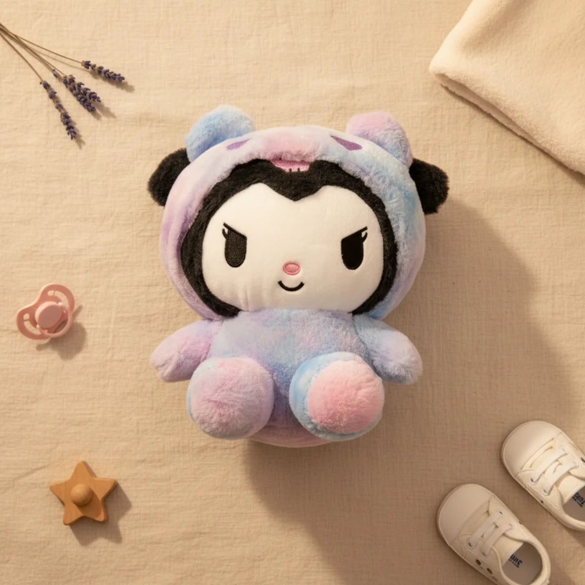 Kuromi galaxy hoodie plush toy flat lay from above on linen background showing lavender blue pink tie-dye hoodie onesie with purple polka dot hood and chunky pink paws with pink pacifier wooden star shape lavender sprigs white baby sneakers and cream muslin cloth