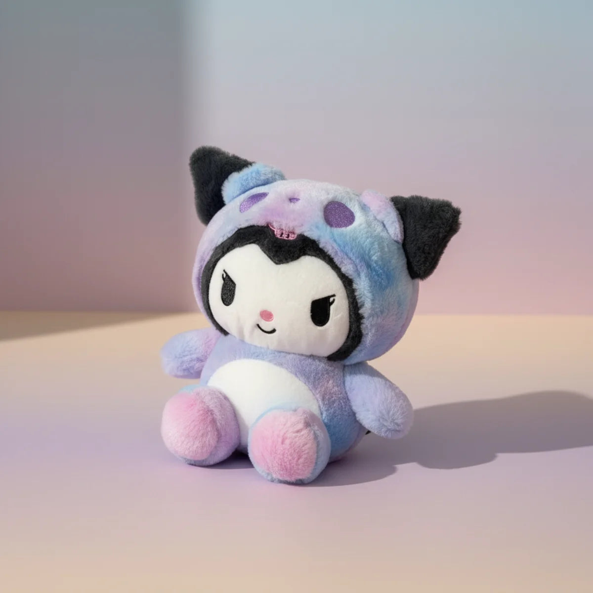 Kuromi galaxy hoodie plush toy studio scene on soft lavender purple gradient background showing Kuromi in tie-dye lavender sky blue bubblegum pink hoodie onesie with purple polka dot hood black bat ears white face and chunky pink paws in sitting pose