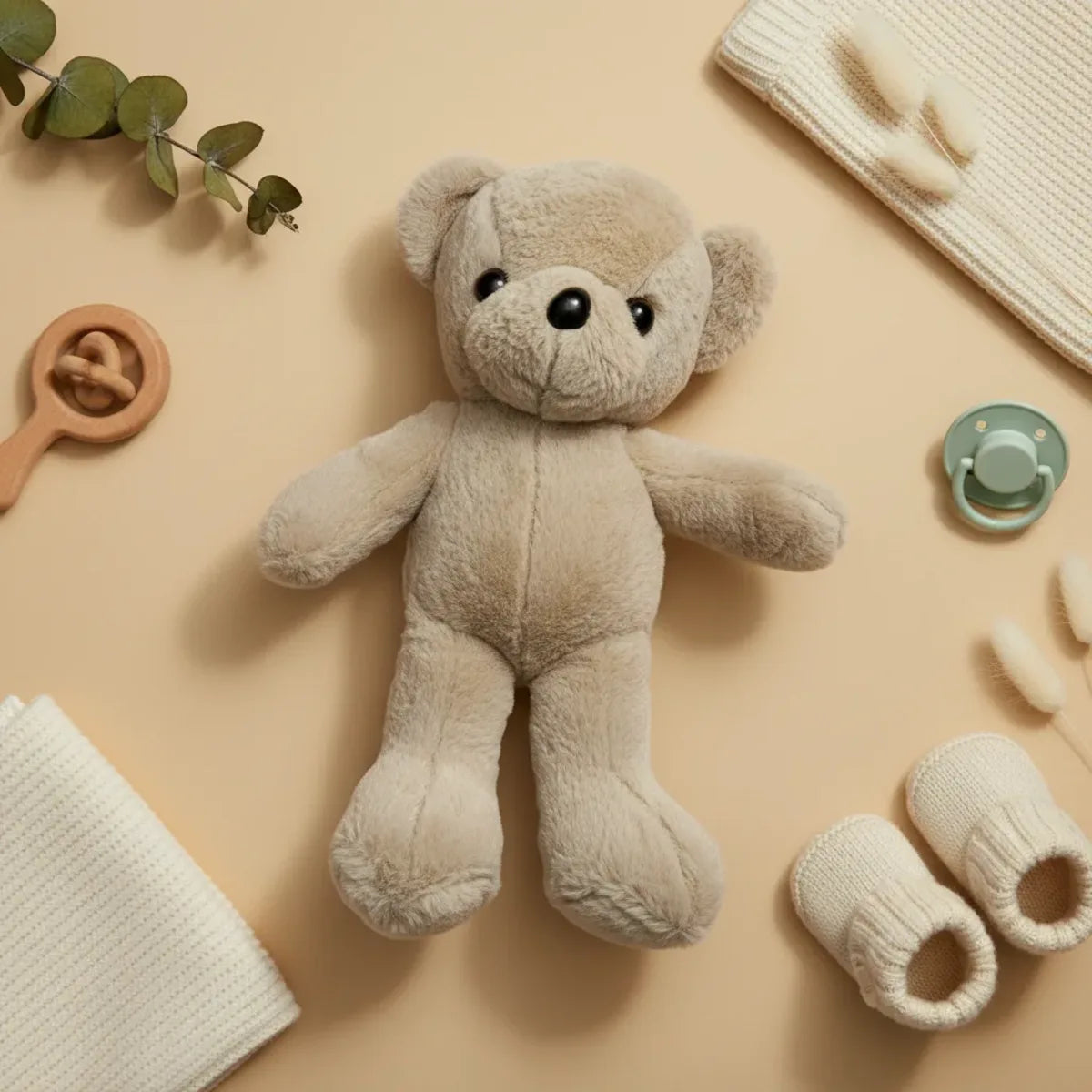Sandy the Beige Minimalist Teddy Bear flat lay with baby booties pacifier and eucalyptus on beige background