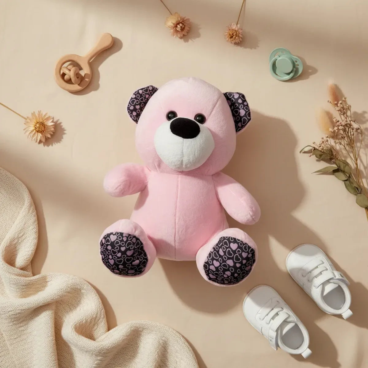 Rosie the Pink Heart Teddy Bear flat lay with baby shoes wooden rattle pacifier and dried flowers on beige background