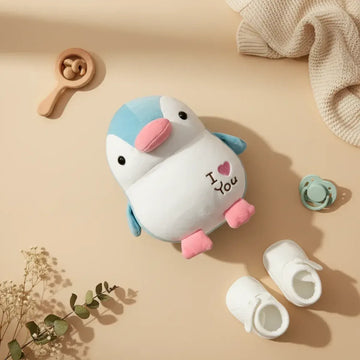 Igloo the I Love You Penguin plush toy flat lay with baby shoes wooden rattle and pacifier on beige background