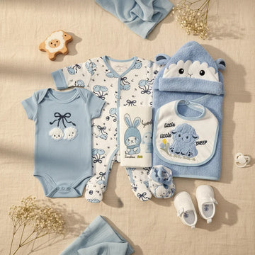 Little Sunshine Newborn Gift Set blue lifestyle flat lay showing sheep bodysuit sleepsuit bib hooded towel booties and accessories on wooden floor with baby shoes wooden sheep toy and dried flowers
