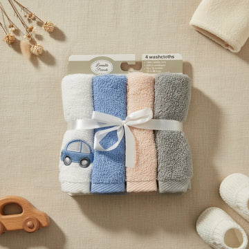 Lovable Friends baby washcloth set of 4 flat lay from above on cream linen background showing four rolled cotton terry washcloths in white sky blue blush pink and grey tied with white satin ribbon bow with embroidered navy car detail in retail packaging beside wooden car toy white knit baby booties cream folded towel and dried pampas grass stems