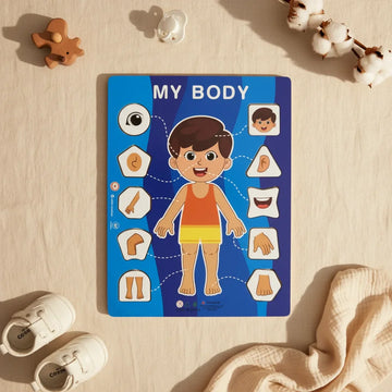 My Body wooden puzzle board boy version flat lay on linen background showing blue board with illustrated smiling boy orange yellow outfit and 10 shaped lift-out body part pieces eye ear nose mouth hand feet arm with wooden bear figurine pacifier and white baby sneakers