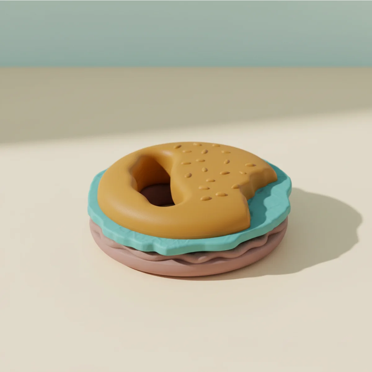 Burger silicone baby teether studio scene showing golden sesame bun top with textured dots and ergonomic ring handle teal wavy lettuce layer and mauve pink bun base stacked on warm cream background with soft teal shadow