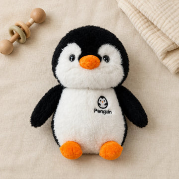 Black-and-white penguin plush with orange beak and feet on cream bedding