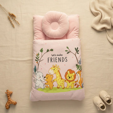 Pink baby sleeping bag flat lay from above on cream linen background showing safari friends print with elephant bear giraffe lion and fox under leafy arch with let's make friends text on soft pink polka dot base with donut head pillow at top beside giraffe teether dried lavender cream knit throw and white baby sneakers