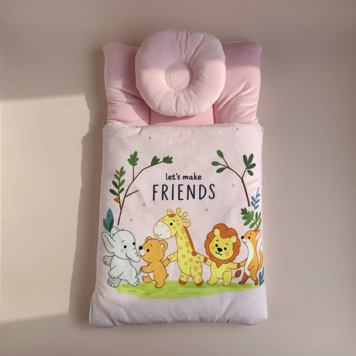 Pink baby sleeping bag studio scene on warm blush pink background showing full top down view of padded quilted pink sleeping bag with let's make friends safari animal print elephant bear giraffe lion fox and donut head support pillow in soft pink showing pink polka dot interior lining at edges