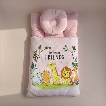 Pink baby sleeping bag studio scene on warm blush pink background showing full top down view of padded quilted pink sleeping bag with let's make friends safari animal print elephant bear giraffe lion fox and donut head support pillow in soft pink showing pink polka dot interior lining at edges