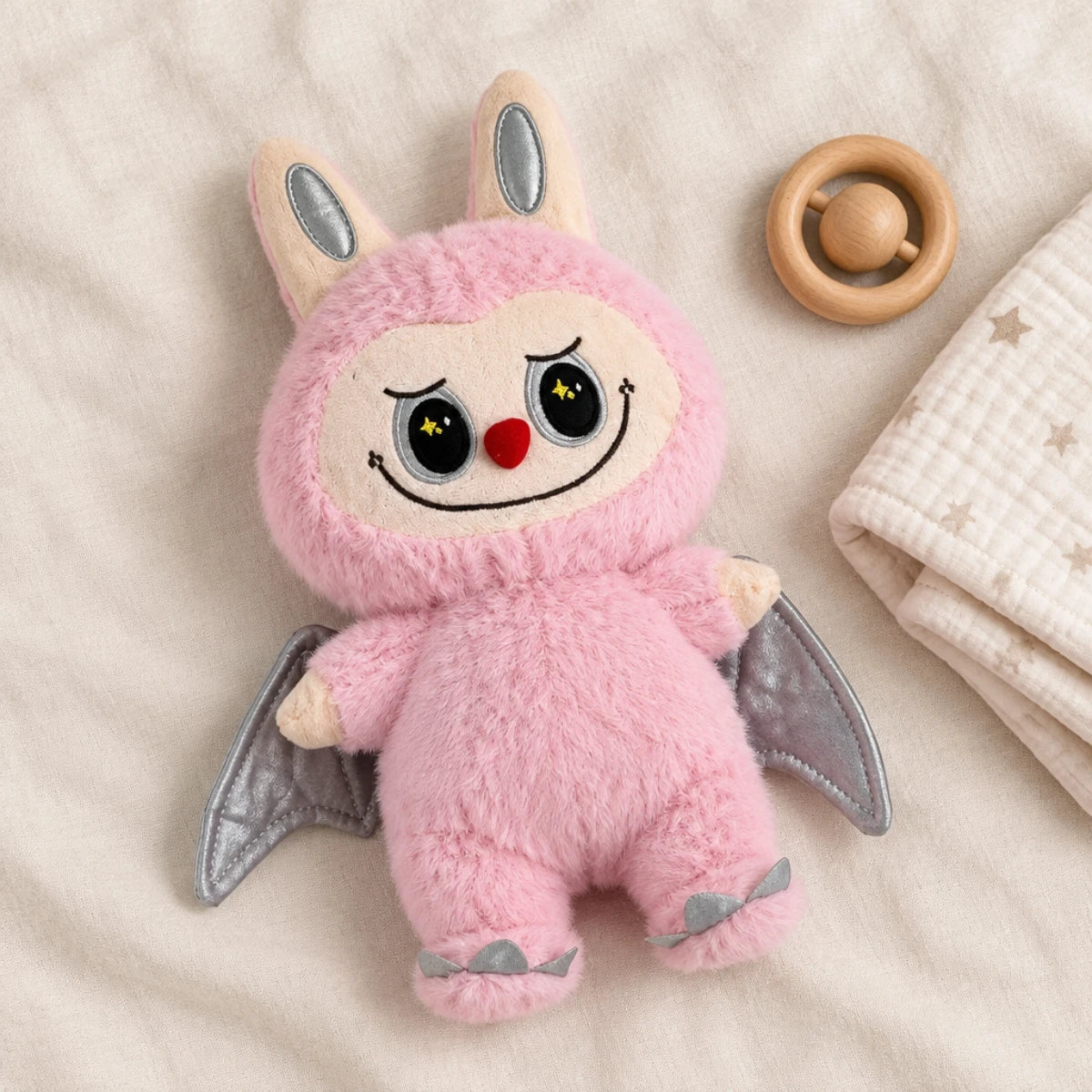 Pink winged plush toy displayed on neutral bedding beside a wooden toy