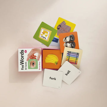 Teeny Baby First Words flash cards studio flat lay showing pink Teeny Baby box with photographic banana orange background yellow duck green background shoes orange background crayons cream background cards and white fork and ball word cards on light pink background