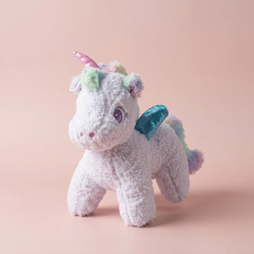 White winged unicorn plush with purple eyes in a soft blush studio