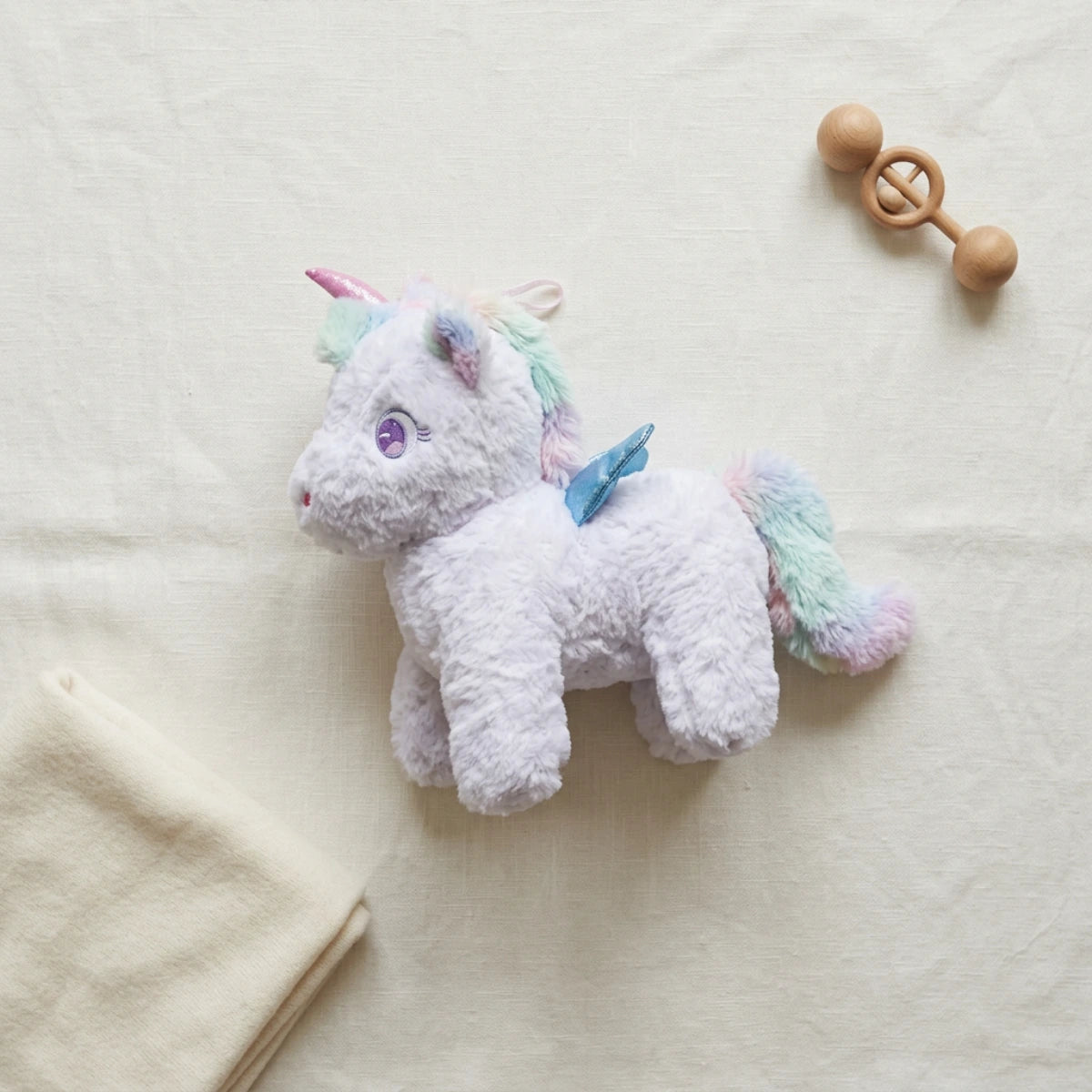 White unicorn plush with pastel mane and tail displayed on ivory linen