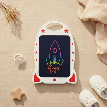 White Rocket Ship 15 inch LCD Writing Tablet showing rainbow colour rocket drawing on screen with red star accents and carry handle on linen background with white pacifier and baby shoes